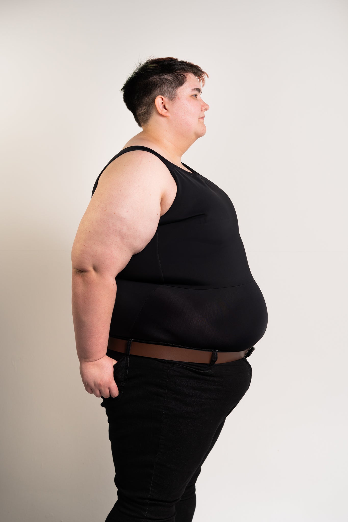 Person wearing a black long chest binder and black trousers against a beige background