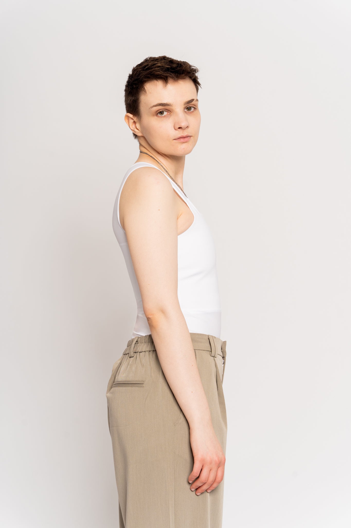 Person wearing a white long chest binder and beige pants against a white background